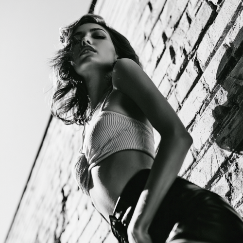 Black and white urban fashion portrait of a woman leaning against a brick wall in dramatic low-angle photography