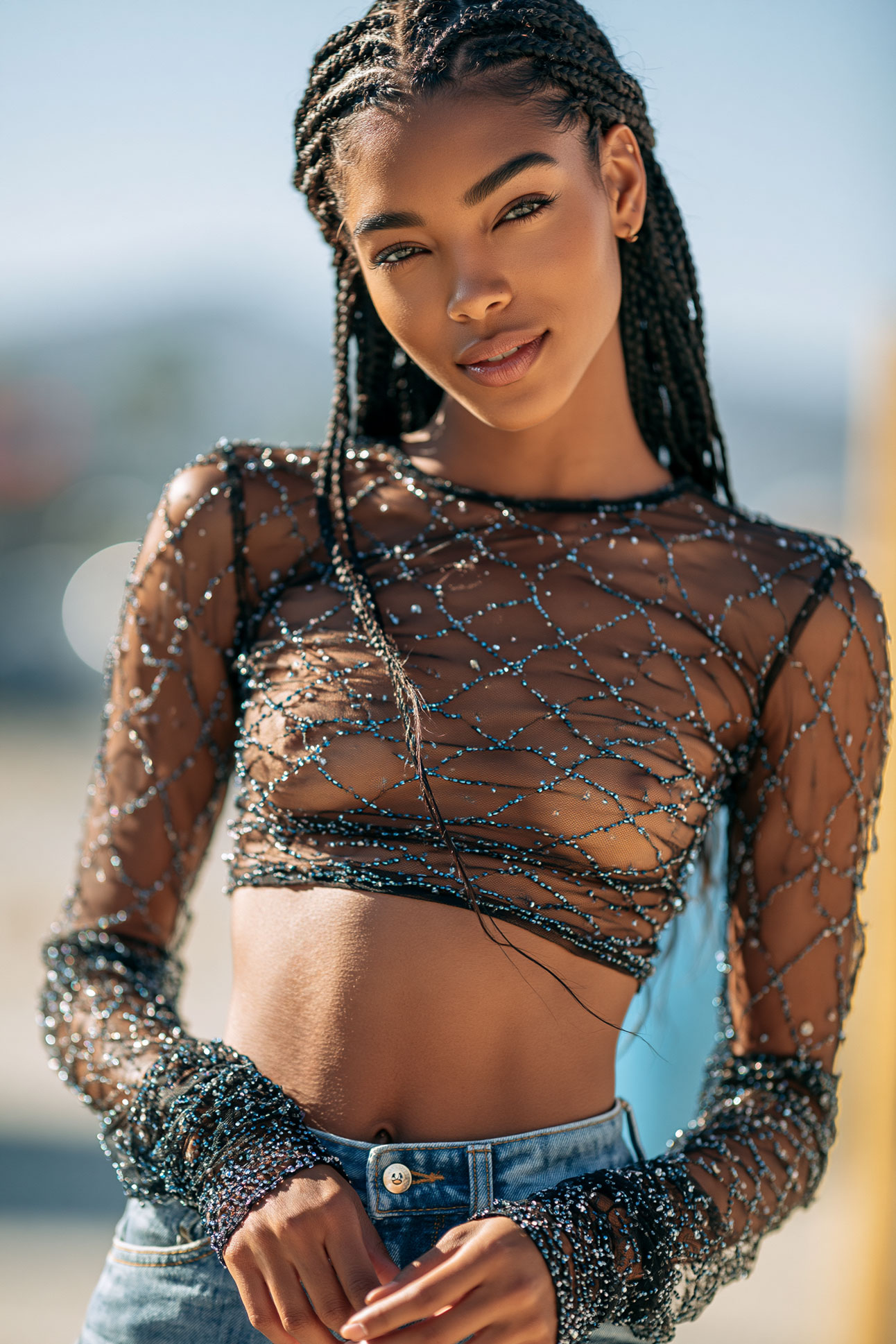Sensual fashion portrait of a glamorous woman wearing a sheer embellished top in natural sunlight.