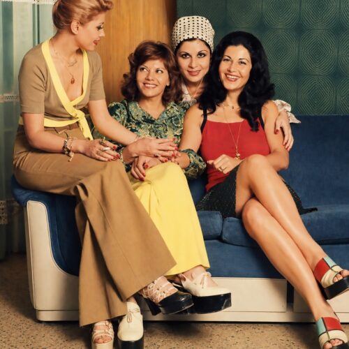 Vintage photograph of four Iranian actresses from the 1960s-70s era sitting together on a blue couch, wearing period costumes and jewelry, embodying mid-century glamour and cultural sophistication.