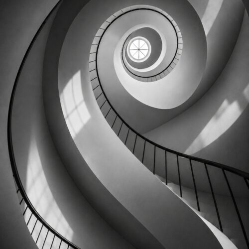 Black and white minimalist spiral staircase with geometric curves and dramatic lighting converging toward a bright center point, architectural wall art poster.