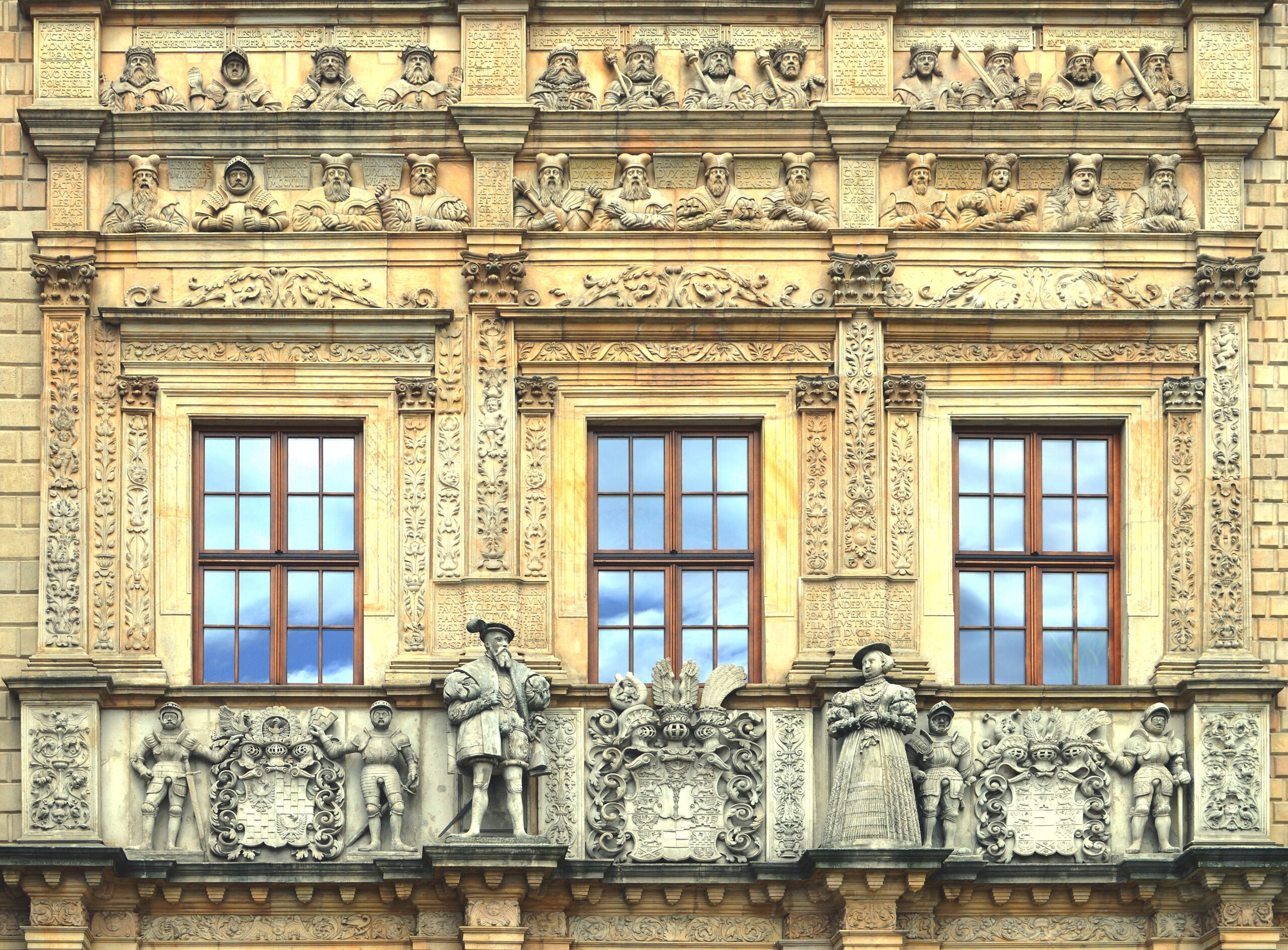 Ornate Renaissance facade of Brzeg Castle with sculptural stone details, classical figureheads, and elaborate carved stonework surrounding tall windows.