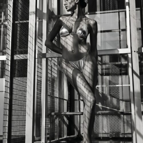 Black-and-white noir portrait of a woman in geometric urban setting with architectural shadows and glass reflections creating dramatic contrast.
