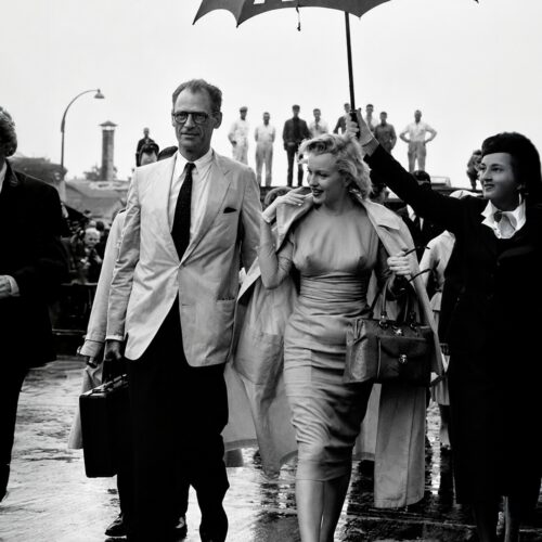 Black-and-white vintage photograph of Marilyn Monroe and Arthur Miller walking under a TWA umbrella at London airport in 1956, iconic Hollywood wall art poster.