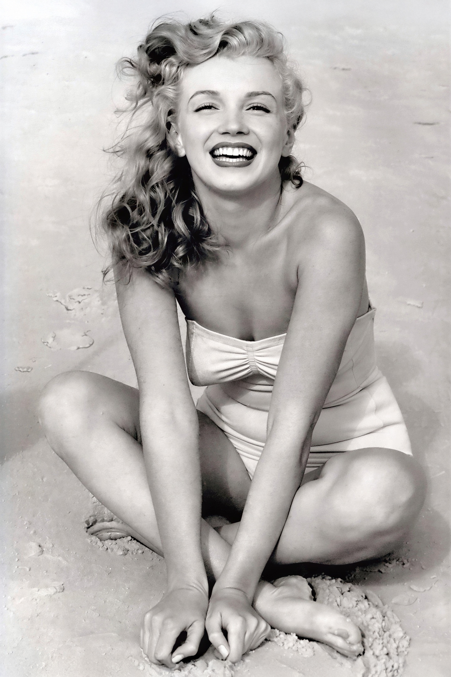 Black and white 1949 vintage portrait of young Marilyn Monroe on Toby Beach by photographer Andre De Dienes, smiling radiantly in classic Hollywood pose.
