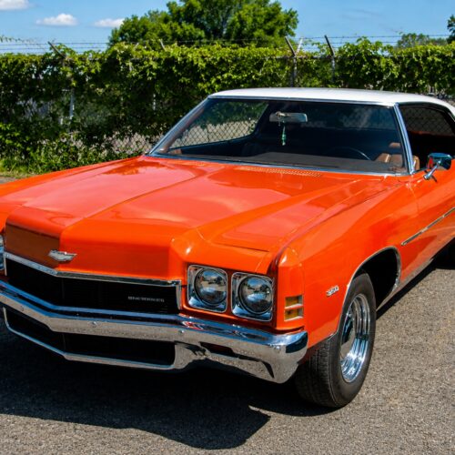 Vibrant photographic poster of a cherry-red 1970s Chevrolet Impala Coupe with chrome details and dual headlights parked in bright daylight.