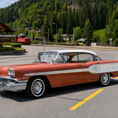 Vintage 1958 Pontiac Star Chief in cherry red and white, photographed in profile with Alpine landscape backdrop, iconic classic American muscle car wall art.