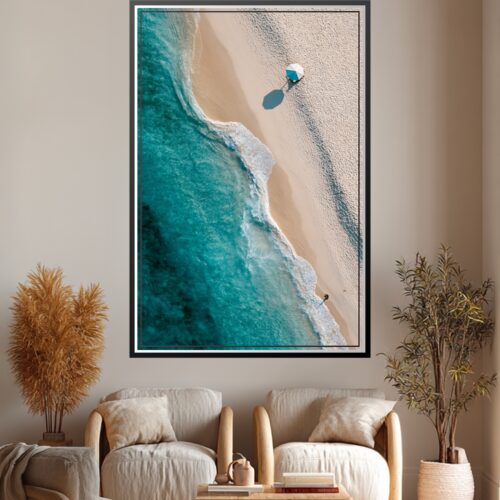Aerial photographic view of a serene beach with turquoise water, white sand, and a figure with blue umbrella casting a shadow on pristine shore.
